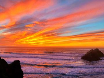 Colorful sunset over the ocean with rocky silhouettes.