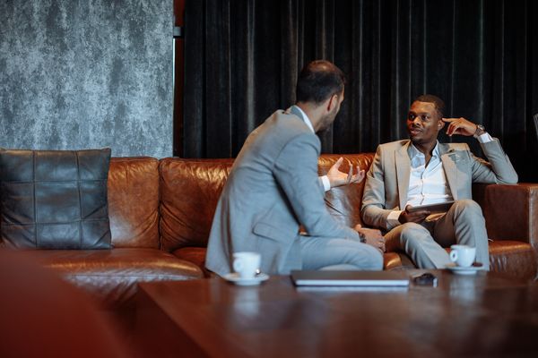 Two businessmen in suits having a discussion on a leather couch.