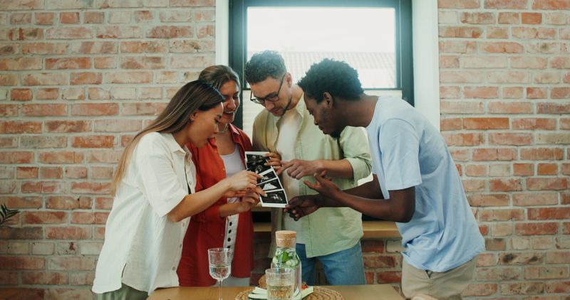 A woman shows her friends ultrasound images sharing the news about her pregnancy, over dinner at home