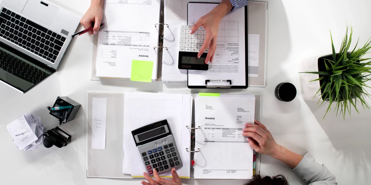 Two people working on invoices and calculations with laptops and calculators.