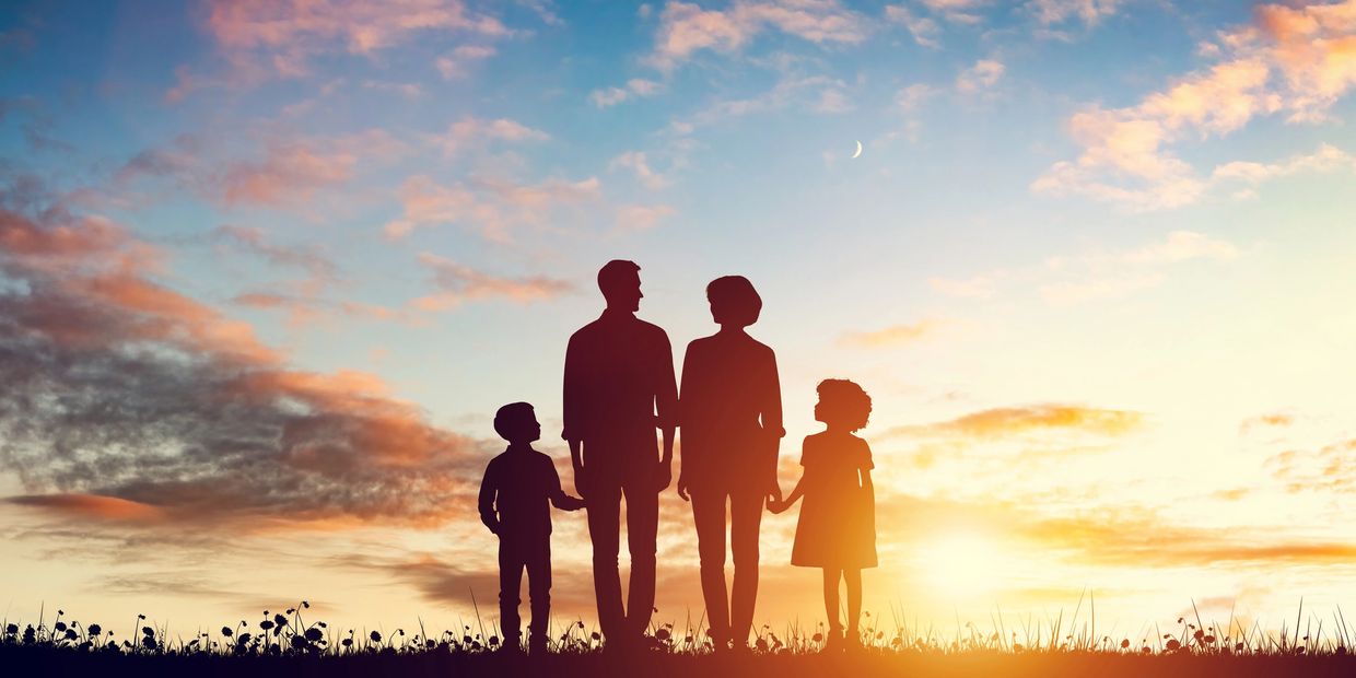 Silhouetted family holding hands at sunset with a crescent moon overhead.