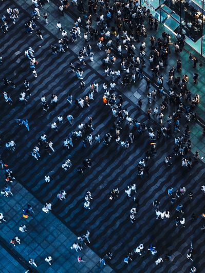 Aerial view of a crowded urban plaza with people walking near a modern glass building.