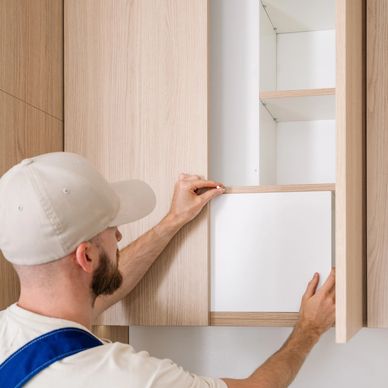 Man installing a wooden shelf inside a kitchen cabinet.