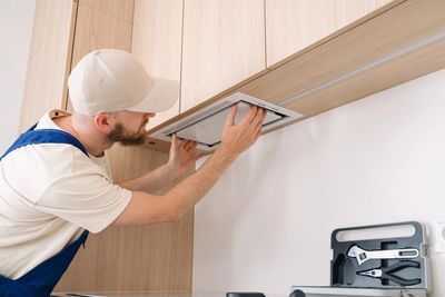 Man installing a kitchen exhaust fan.