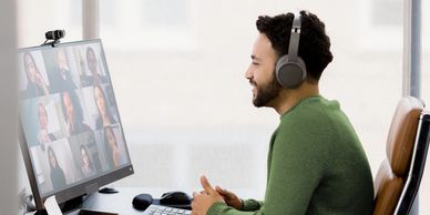 Man with headphones engaged in a video conference at his desk.