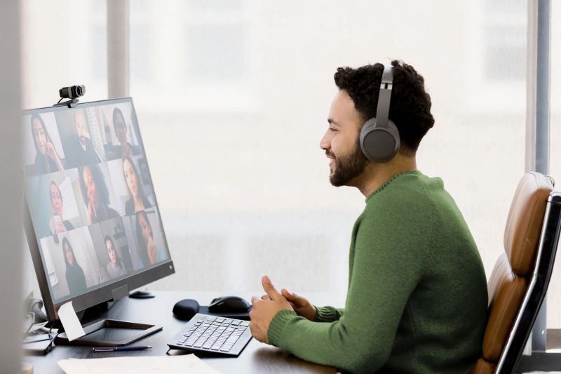 Smiling man participates in a virtual meeting on his computer.  Diverse group of people visible on screen.