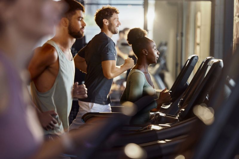 African American female athlete jogging during sports training on treadmill among other athletes in a gym.
