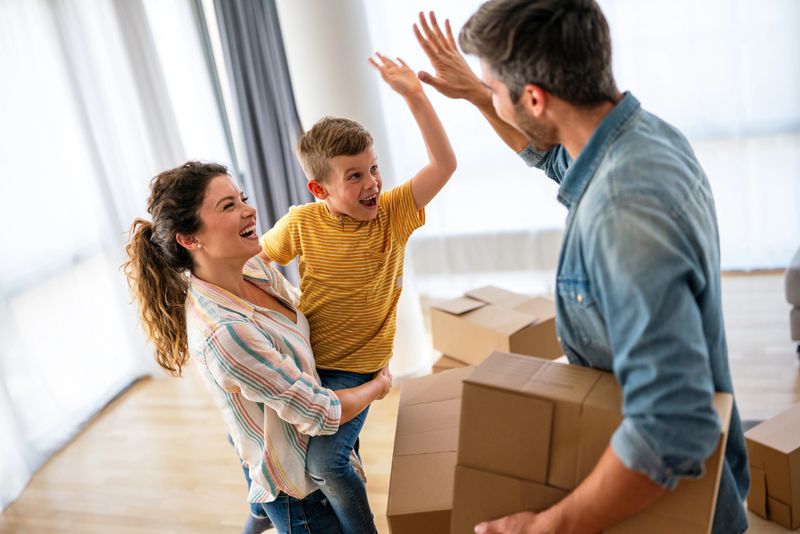 Happy young Caucasian family with small son have fun on relocation day to new house or apartment. Smiling man and woman enjoy unpacking with child moving to own home. Rent, mortgage concept