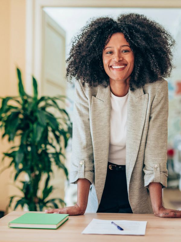 Confident woman leaning on a desk with a smile, ready to work.