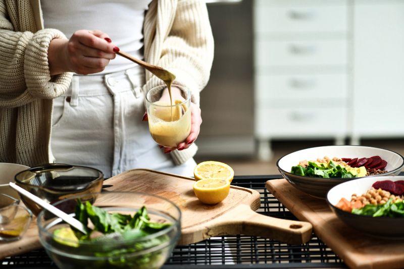 Female Preparing and Stirring Salad Dressing in Glass For Colorful Buddha Bowls