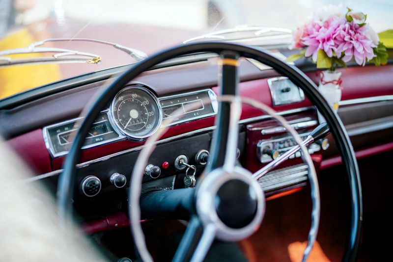 Retro interior steering wheel and dashboard of a vintage car, featuring floral decor and vibrant colors, presenting a nostalgic design aesthetic.