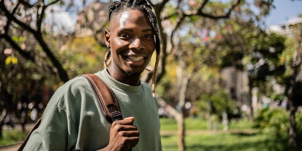 Smiling young man with braided hair and braces outdoors with a backpack.