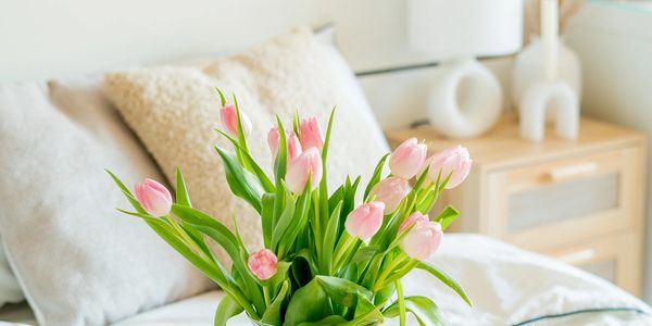 A cozy bedroom tray with pink tulips, a candle, and a cup of coffee.