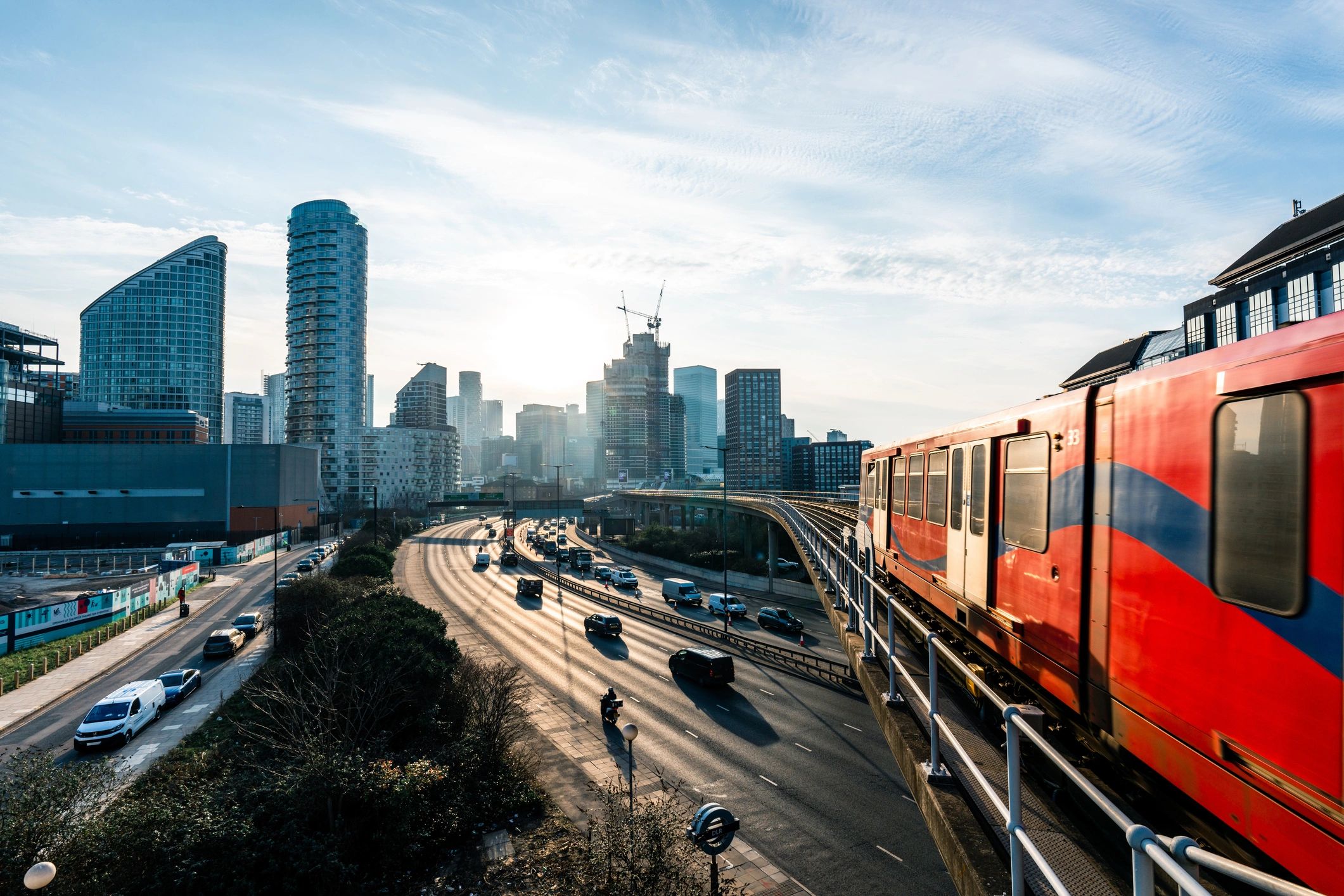 Red train on elevated tracks, skyscrapers in the background and a busy road below. 