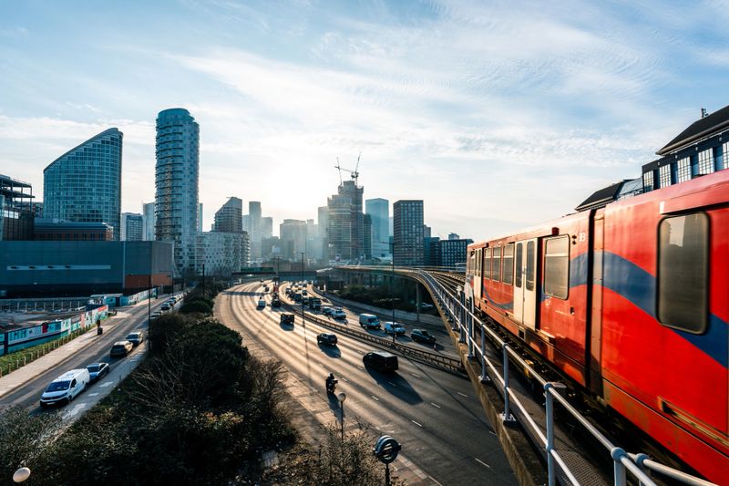 Red and blue commuter train passing over busy highway in london, england, during sunset