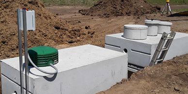 Concrete septic tanks being installed beside a house on a clear day.