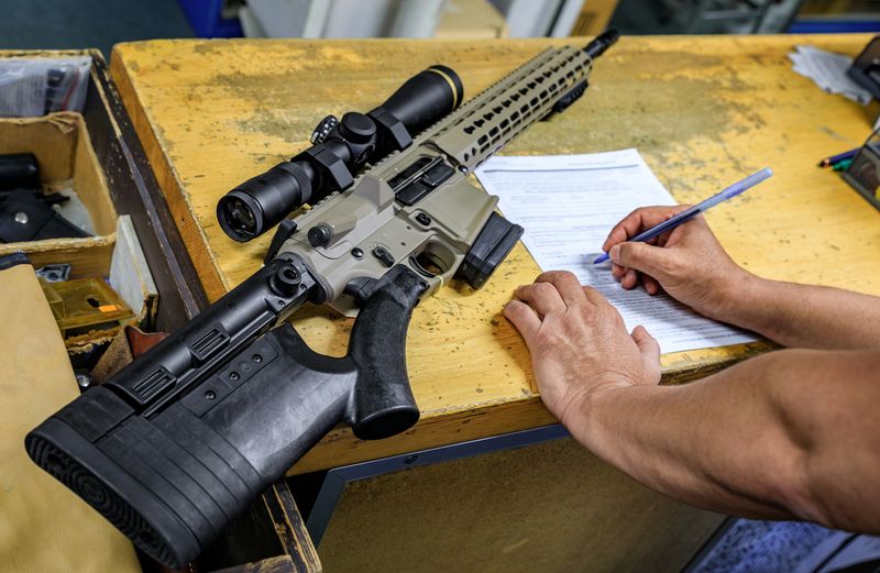 California gun shop: male buyer signs the paperwork beside a modern AR-15 rifle with a scope, verifying purchase in compliance with state regulations