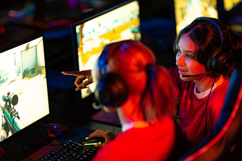 Multiracial female only cybersport gamers expressing success while raising hands up and smiling during participation in esports tournament in computer club