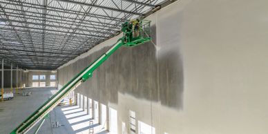 Workers painting a large indoor wall using a lift.