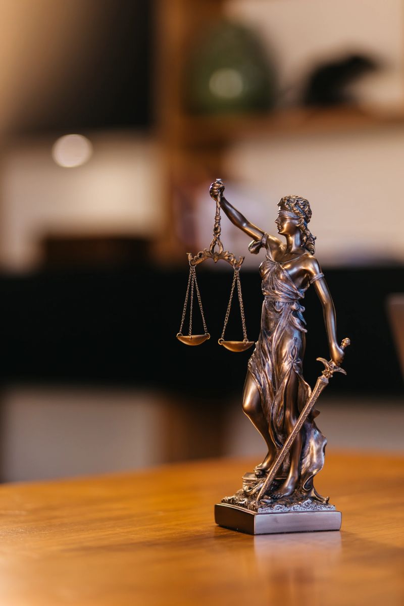 A statue of Justice on a lawyer's desk with a laptop in the evening, under warm lighting. Concept justice, professionalism, and legal expertise.