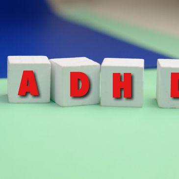 White blocks spelling ADHD with red letters on a green and blue background.