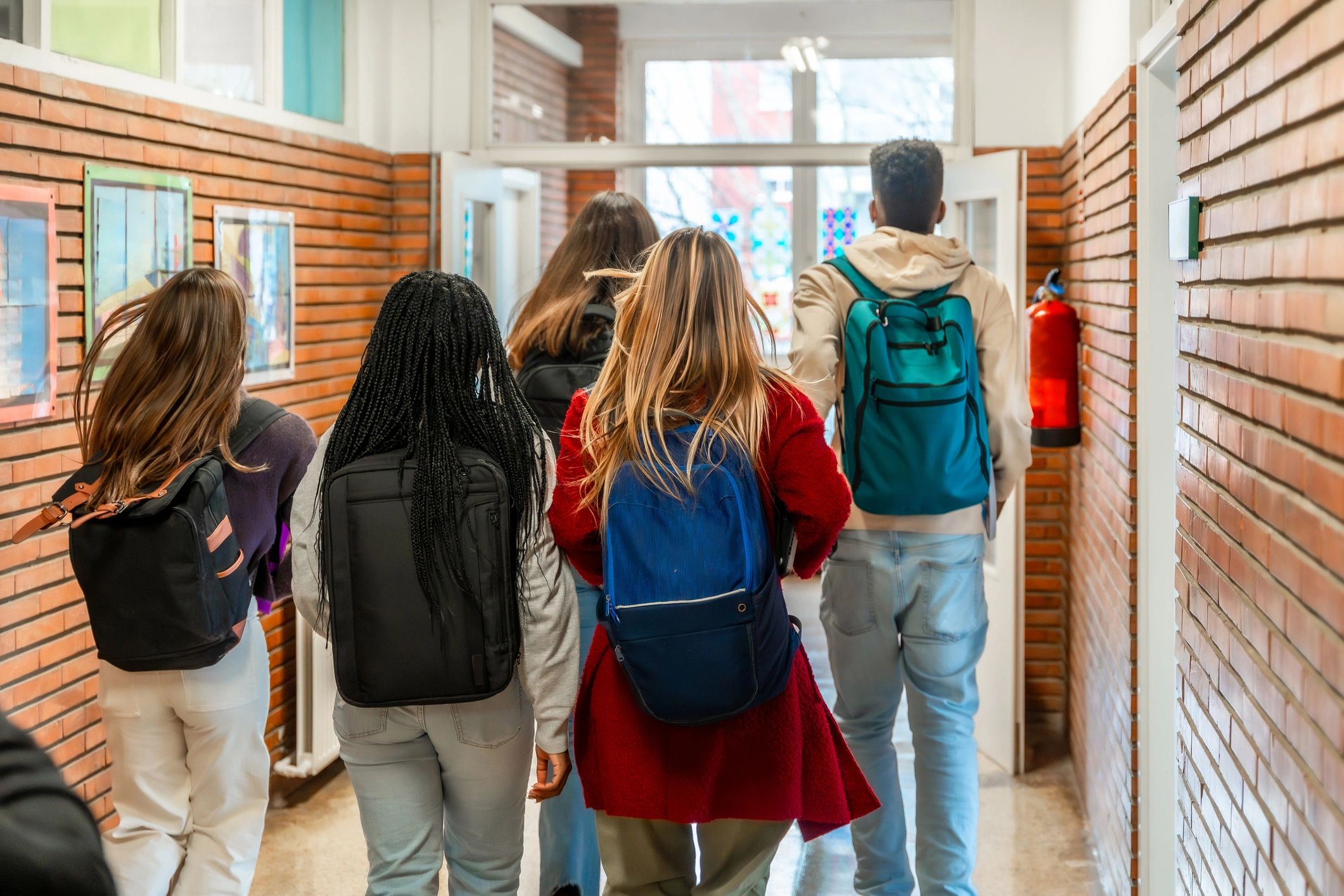 Group of students walking down a school hallway with backpacks.
