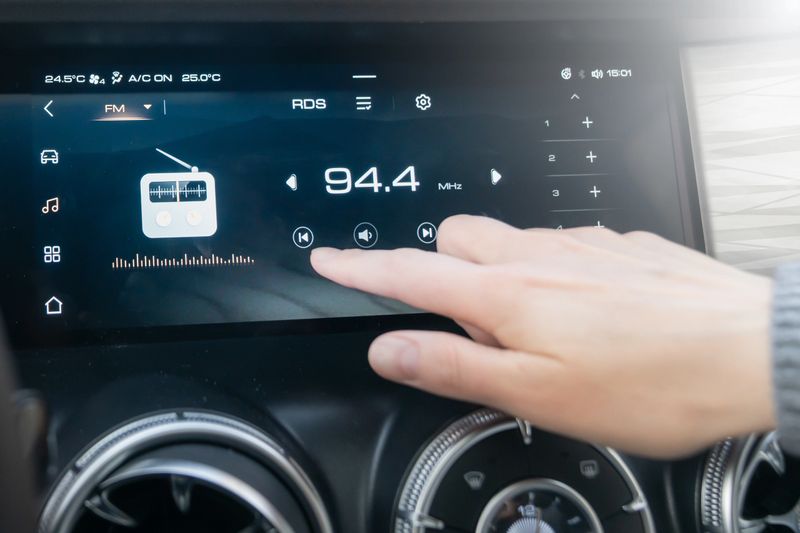 The passenger controls the radio on the car's touchscreen with his finger. An individual adjusts the radio on a sleek car dashboard touchscreen, highlighting convenience and technology