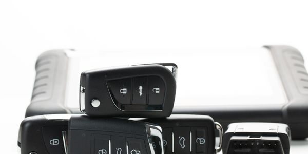 Automotive keys, fob, smart key, prox key and an automotive diagnostic tool on a white surface. By Rock Solid Locksmith
