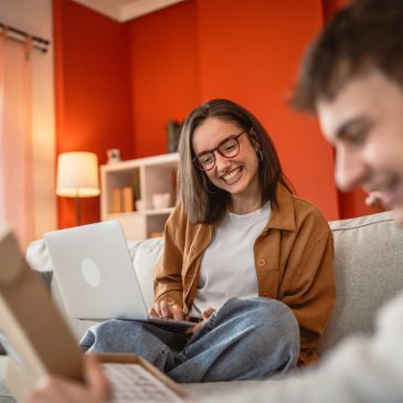 Young woman smiling and working on a laptop in a cozy living room.