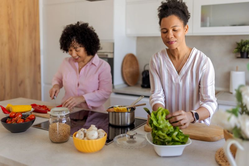A candid moment of friendship unfolds in a beautifully decorated kitchen, where two African American women enjoy cooking together. Their cheerful expressions and the inviting ambiance of the space make this a heartwarming scene of togetherness and joy.