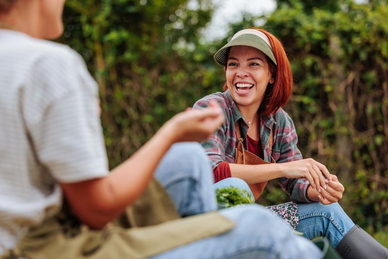 Two young adults enjoying a cheerful conversation while taking a break from gardening in a lush, green outdoor setting
