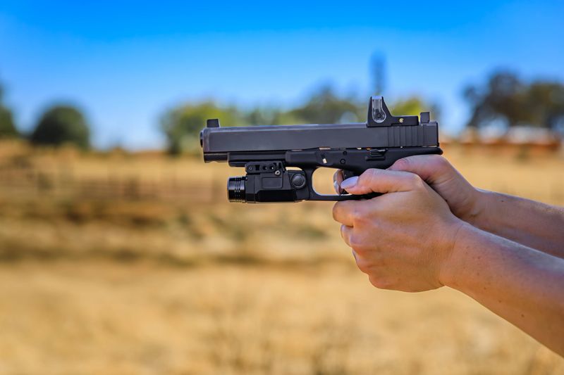 Woman s hand holding a modern semi automatic .40 caliber pistol with a red dot laser sight at an outdoor shooting range in Placerville, California