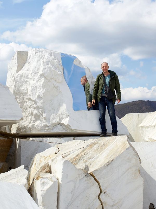 Man standing next to a large white marble block with a reflective surface.