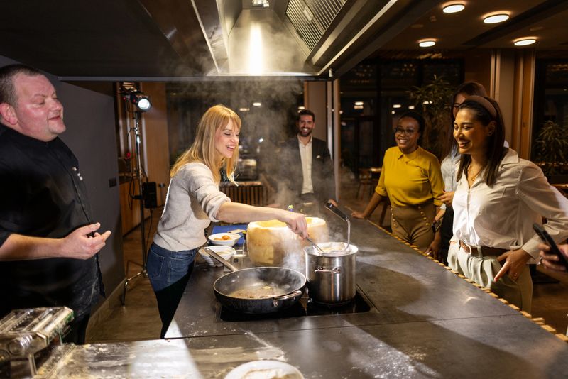 The chef preparing pasta with pecorino cheese in front of the multiracial group of guests in luxury hotel