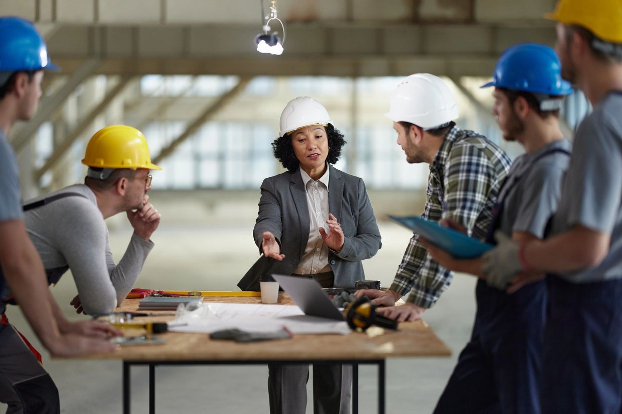 Female engineer discusses plans with construction workers at a site meeting.