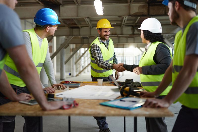 Happy manual worker reached a successful agreement with female building contractor next to their colleagues at construction site.