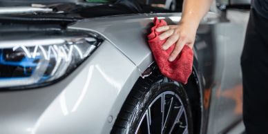 Person cleaning a car's front fender with a red cloth.