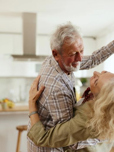 Elderly couple dancing closely in a bright, cozy kitchen.