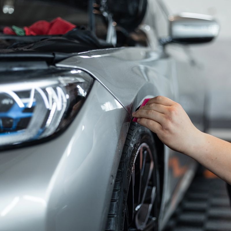 Professional man covers car with protective film and cuts with blade in detailing service. Car protection and care