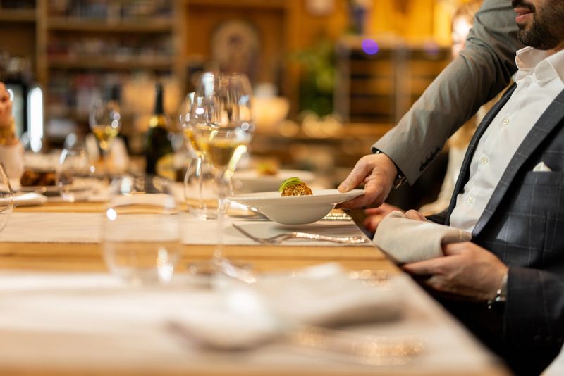Close up shot of unrecognizable waiter serving food to multiracial group of guests in a luxurious hotel restaurant