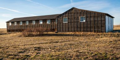 A large barn-like structure covered with black tarp on a dry grassy field.