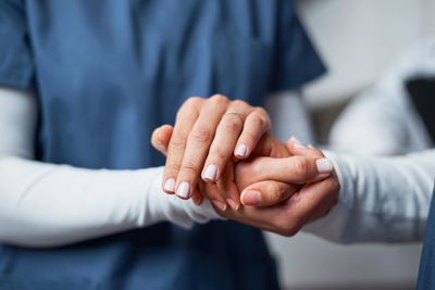 A healthcare worker gently holding a patient's hand in support.