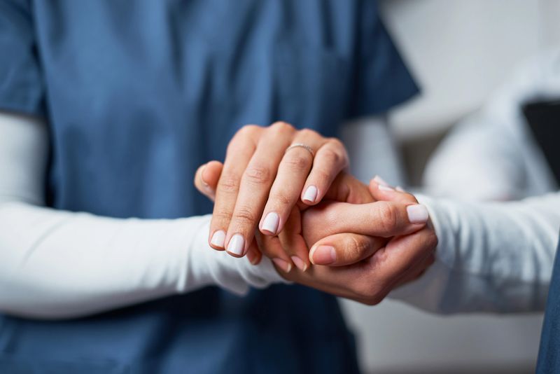 A professional nurse provides emotional support by gently holding a patient's hand, symbolizing care and empathy. This closeup image communicates trust, kindness, and the human connection within the medical field.