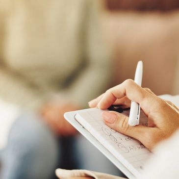 Person writing notes on a clipboard during a counseling session.
