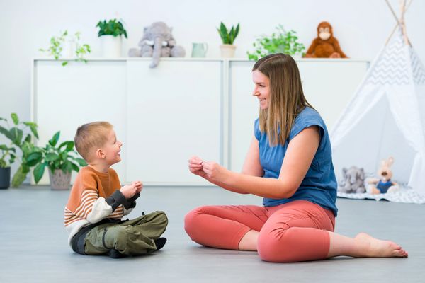 soft colors, gentle background therapist sitting on floor with child using sign language together