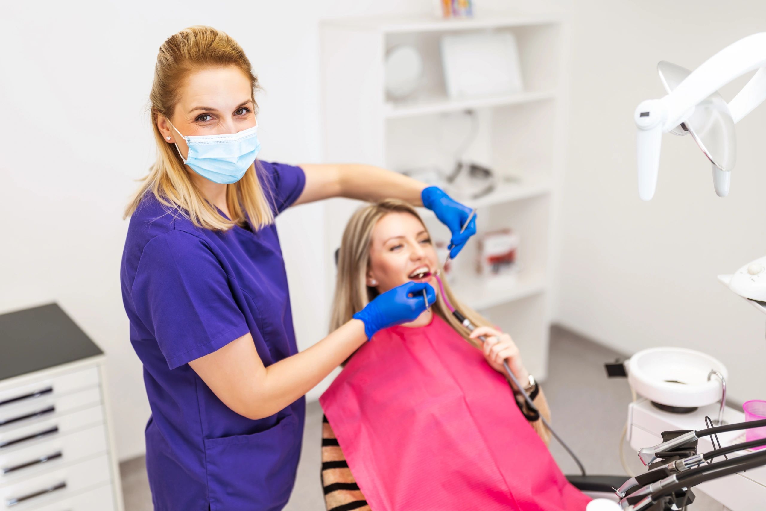 Dentist in purple scrubs treating patient with dental tools.