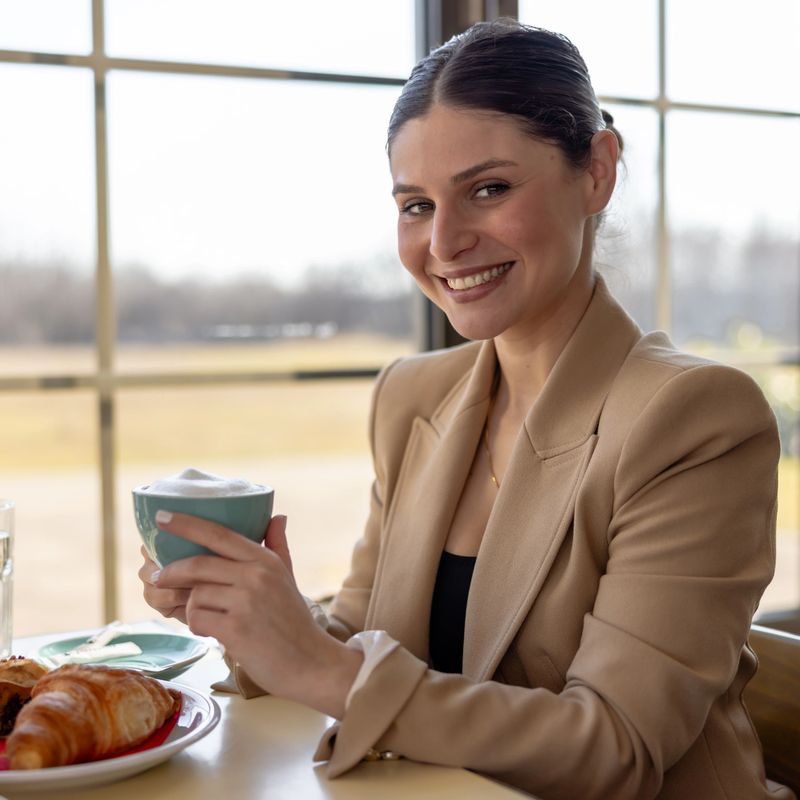 Beautiful Caucasian woman smiling and holding a cup of coffee while sitting by the window in a cafe