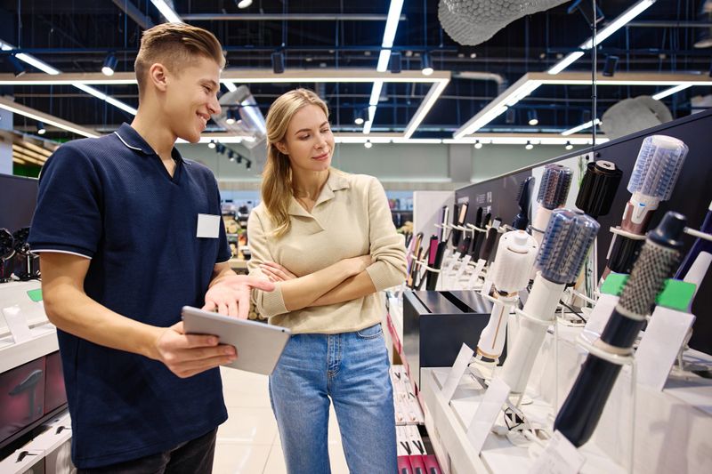 A happy customer exploring hair styling tools with a knowledgeable salesperson in a bright, modern store setting