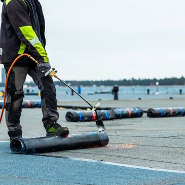 Worker using a blowtorch to install roofing material on a flat roof.
