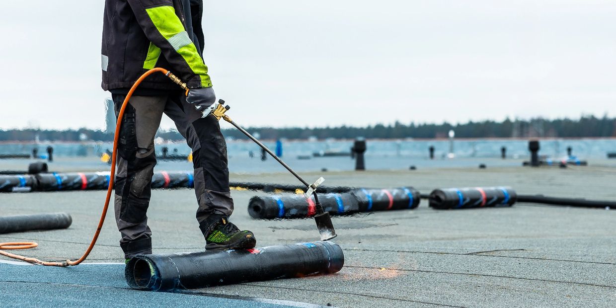 Worker using a torch to apply roofing material on a flat roof.